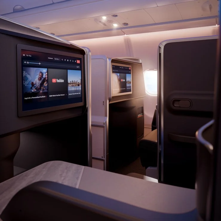 Interior view of a modern airplane cabin featuring individual entertainment screens showing YouTube and other content options.