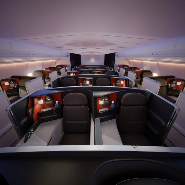 Interior view of a modern airplane cabin featuring business class seats arranged in a spacious layout. Each seat is equipped with personal entertainment systems and privacy dividers.