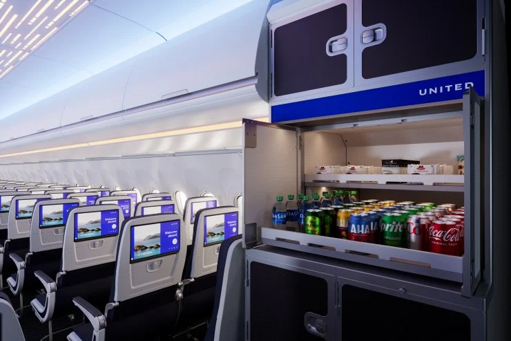 Interior of a United Airlines airplane showing empty passenger seats with personal screens, and an open beverage cart stocked with various drinks.