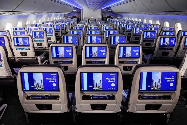 Interior view of an airplane cabin with multiple rows of seats equipped with individual screens displaying 'Welcome aboard' and flight information.