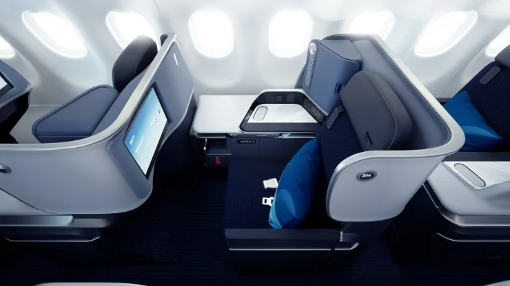 Aerial view of a modern airplane cabin featuring spacious business class seats with individual screens and blue pillows.