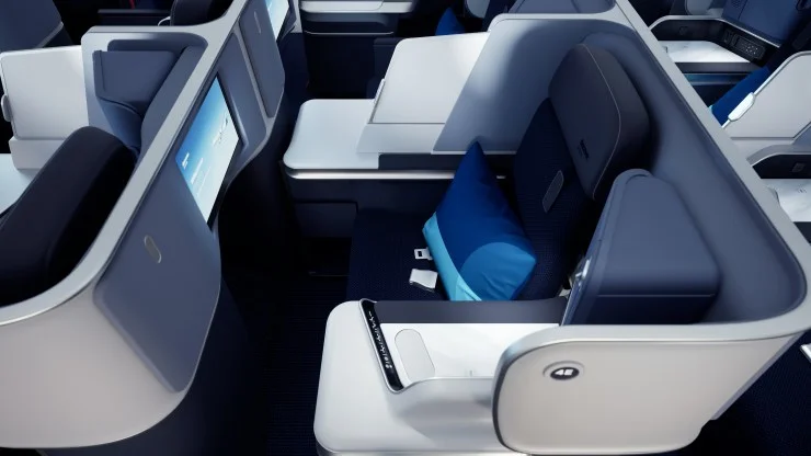 Interior view of a modern airline business class seat with a sleek design, featuring a blue pillow and a personal screen.