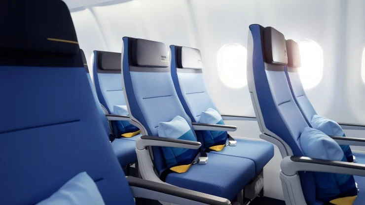 Interior view of an airplane cabin showcasing blue seats with headrests and pillows, illuminated by natural light from the windows.