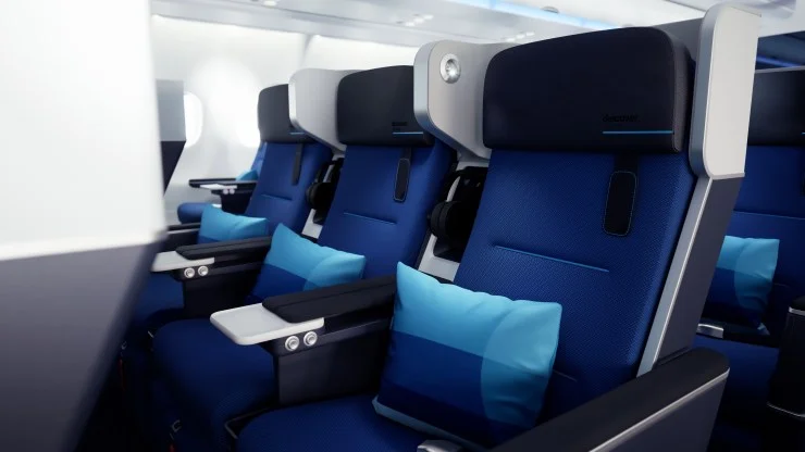 Interior view of an airplane seating area featuring blue ergonomic seats with headrests and small pillows, arranged in a row.