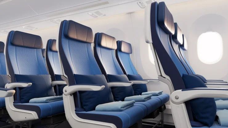 Interior of an airplane showing a row of blue fabric seats with headrests and small pillows, next to windows.