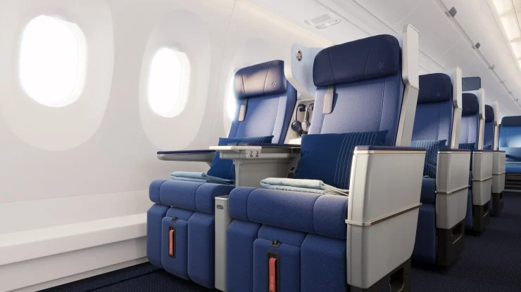 Interior view of an airplane cabin showing blue seats with headrests and decorative pillows, alongside large windows.