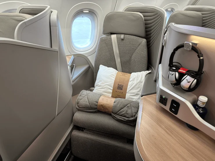Interior view of Etihad's Airbus A321LR Business Class seat featuring a plush design with a pillow and blanket, alongside a personal touchscreen and headphones.