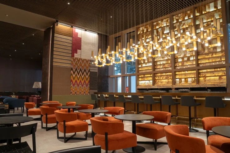 Interior view of the LATAM Signature Lounge in Lima featuring modern furnishings, vibrant orange chairs, and a stylish bar area with pendant lighting.