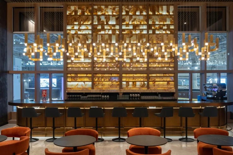 Interior view of the LATAM Lounge at Jorge Chávez International Airport, featuring a stylish bar area with modern lighting, seating, and a warm color palette.
