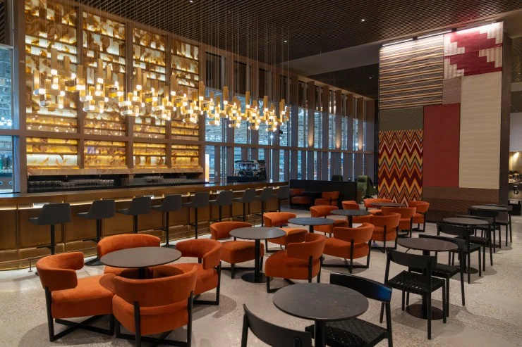 Interior view of the LATAM Lounge at Jorge Chávez International Airport, featuring a modern design with orange armchairs, a bar area, and decorative wall elements.