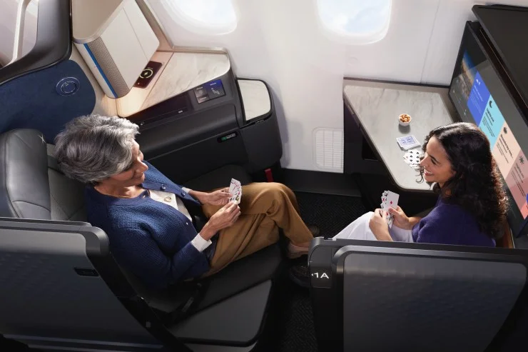 Two passengers enjoying a card game in a United Airlines Polaris Studio suite aboard a Boeing 787-9 Dreamliner, featuring comfortable seating and a personal screen.