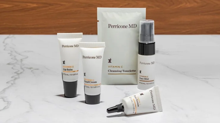 Perricone MD skincare kit featuring lip balm, hand cream, cleansing towelette, face mist, and eye serum arranged on a marble surface.