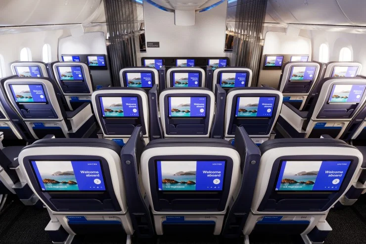 Interior view of United Airlines' economy class seating arrangement with 'Welcome aboard' screen displays.