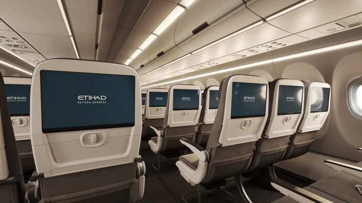 Interior view of an Etihad Airways narrowbody aircraft featuring Economy Class seats with personal monitors displaying the airline's logo.