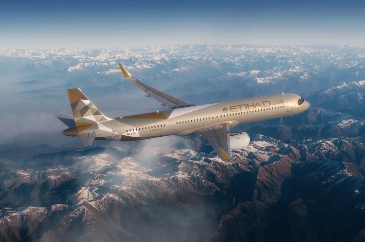 An Etihad Airways A321LR aircraft flying over a mountainous landscape, showcasing its distinctive livery with golden accents.