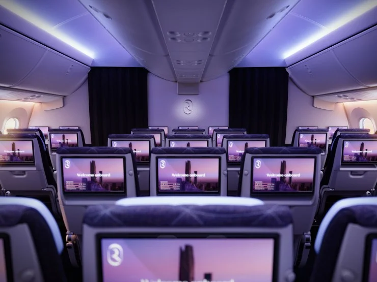 Interior view of a modern airline cabin with rows of seats and individual entertainment screens, showcasing a welcoming ambiance with soft lighting.