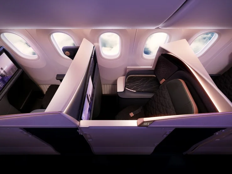 Aerial view of a luxurious airplane cabin interior featuring spacious Business Class seats with privacy dividers, backlit accents, and large windows overlooking the clouds.