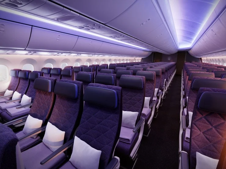 Interior view of a premium economy cabin featuring purple and dark indigo seats, with plush headrests and cushioned neck pillows, softly lit by ambient lighting.