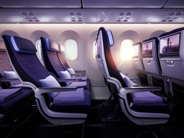 Interior view of a modern airplane seating layout in a cabin, featuring purple upholstered seats with headrests, personal screens, and large windows, creating a spacious and luxurious atmosphere.