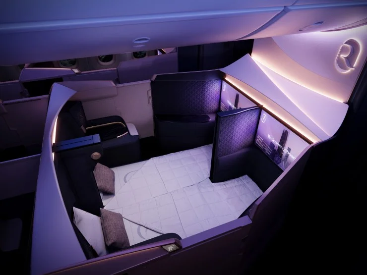 Interior view of a luxurious airline suite showing a spacious seating area with a double bed arrangement, ambient lighting, and modern design elements.