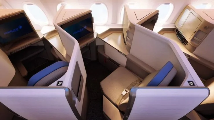 Interior of a Malaysia Airlines 737-10 MAX Business Class cabin featuring lie-flat seats, privacy partitions, and personal entertainment screens.